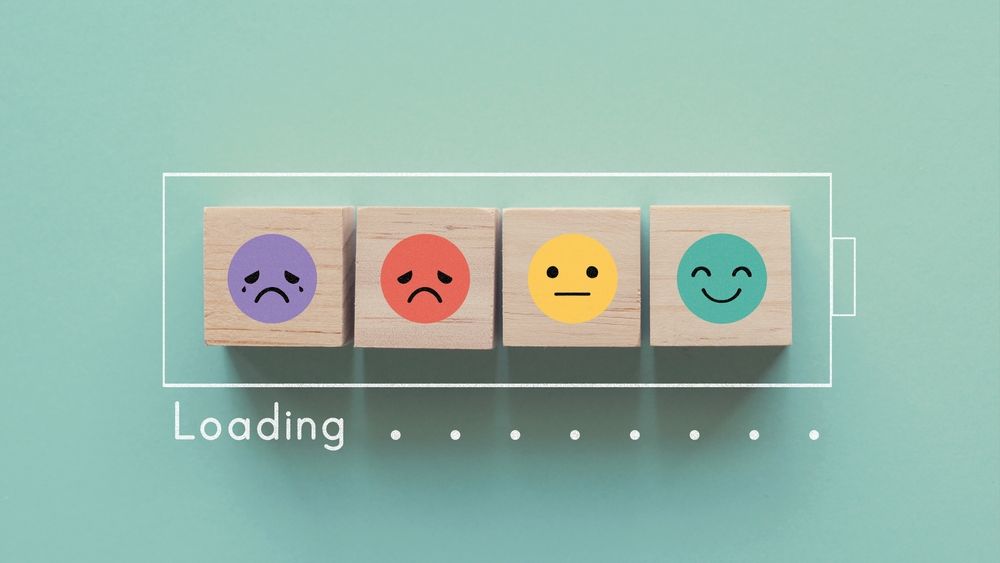 Four wooden blocks with emoji faces representing sad, angry, neutral, and happy emotions in a loading bar.