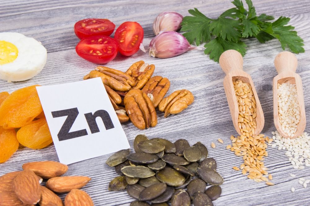 Various foods rich in zinc, including pecans, pumpkin seeds, almonds, eggs, tomatoes, garlic, and grains.