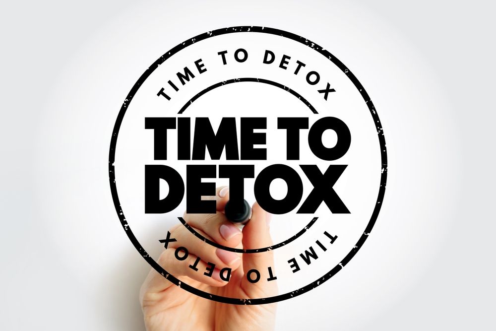 Hand holding a black marker, writing “TIME TO DETOX” inside a circular stamp.