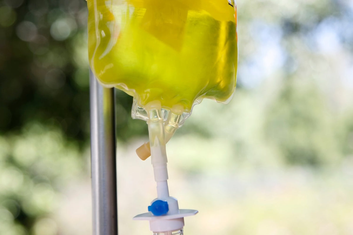 IV bag filled with yellow liquid, hanging from a metal pole, blurred green background.