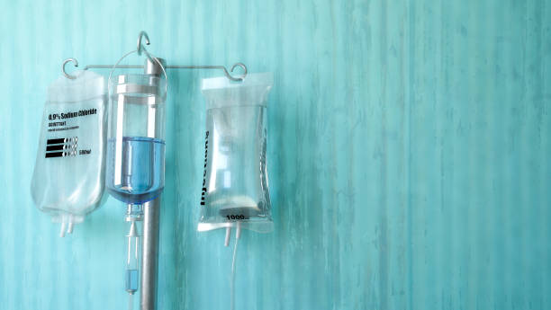 IV drip setup with bags hanging on a stand, against a blue-green wall.