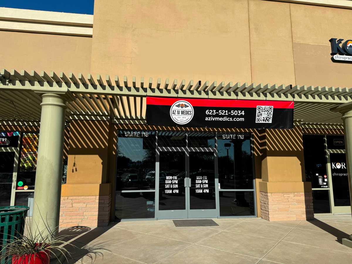 Exterior of a business with a black and red sign above the door. Building is beige with a covered entrance.
