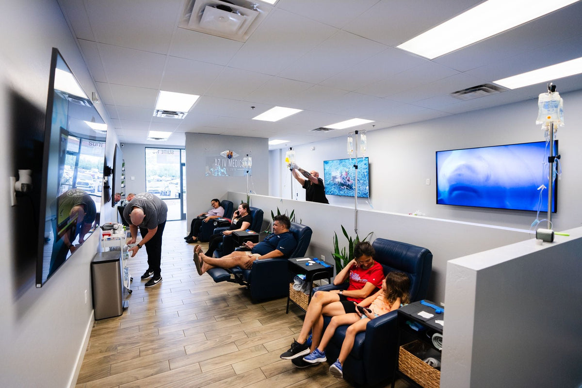People receiving IV drips in a clinic; reclining chairs, TVs, and medical staff present.