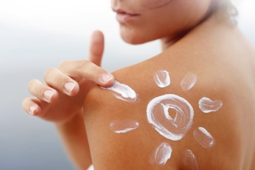 Woman applying sunscreen in a sun shape on her shoulder, tanned skin, outdoors.
