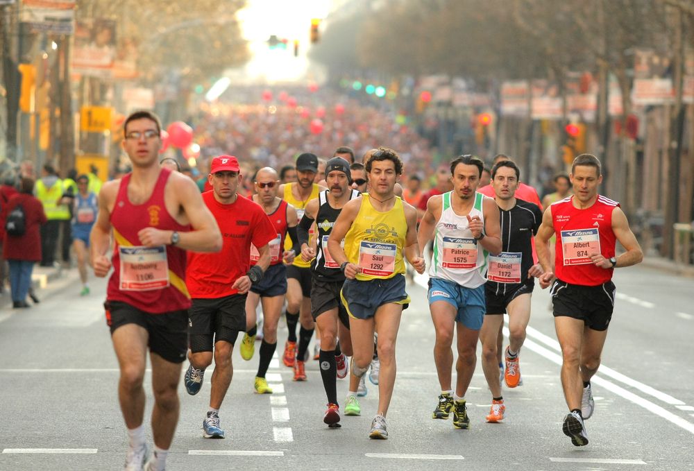 Marathon runners in brightly colored shirts run down a city street.