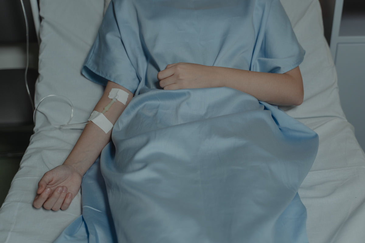 Person in a blue hospital gown lies in bed with IV in arm.