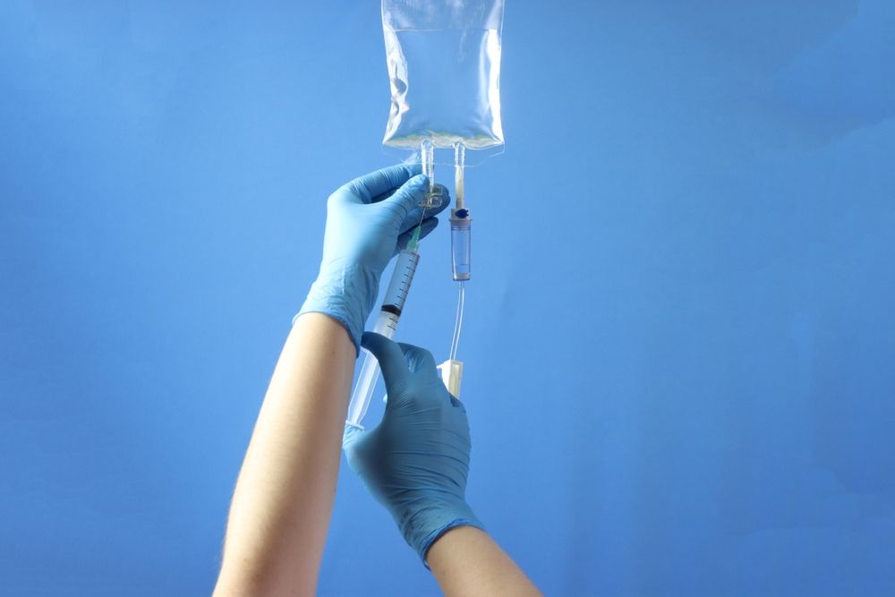 Hands in blue gloves manipulating an IV bag and tubing, preparing an intravenous infusion.