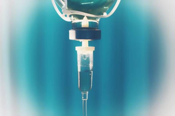IV drip bag with liquid dripping into a tube, against a blue background.