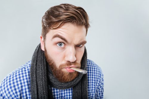Man with beard and scarf taking temperature with thermometer, looking ill.