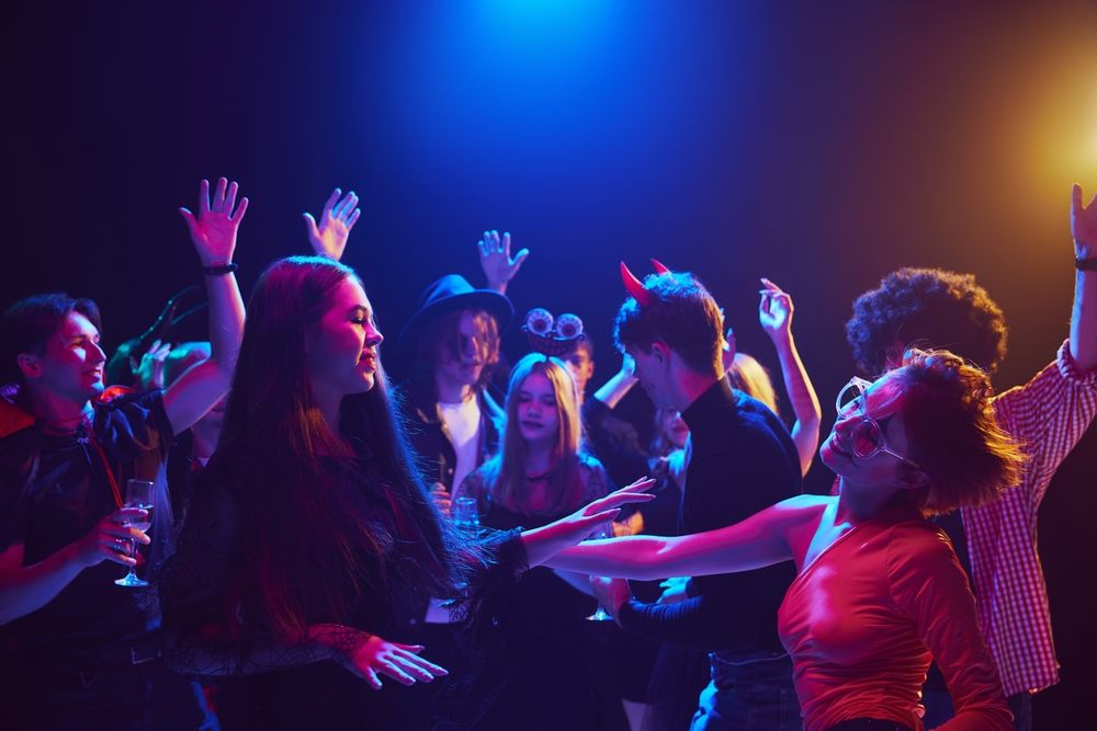 People dancing at a party under blue and red lights. Some have horns and costumes.
