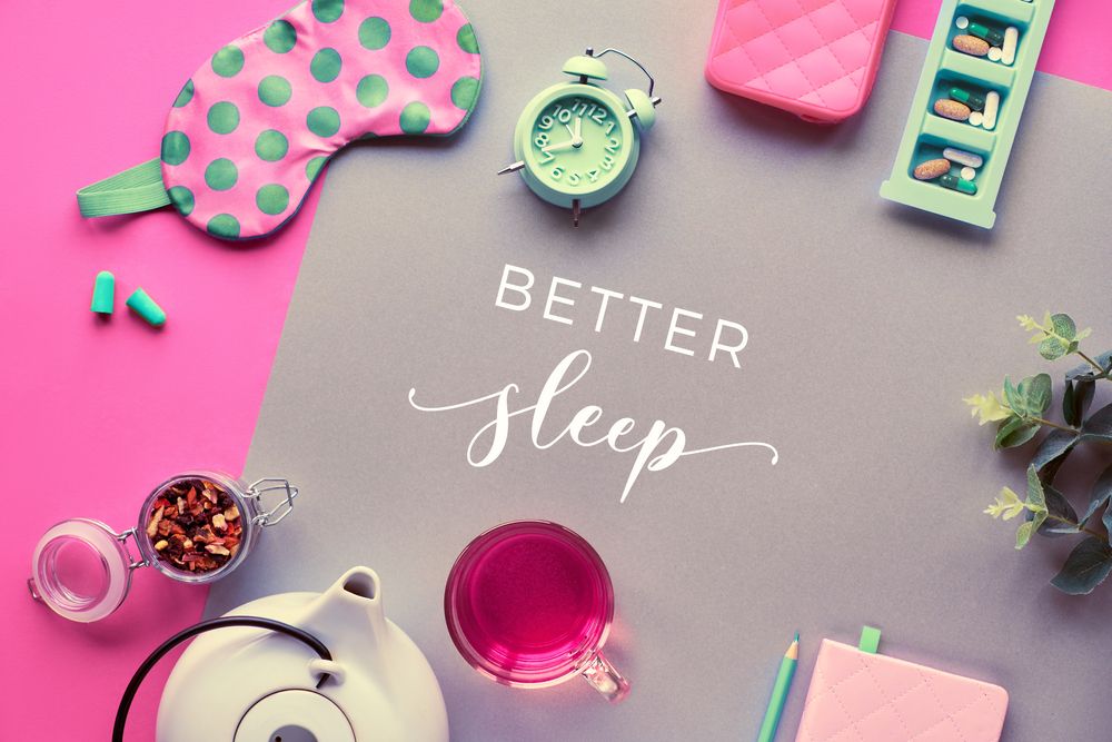 Pink and gray flat lay with sleep mask, alarm clock, tea, and pills. Text: Better Sleep.