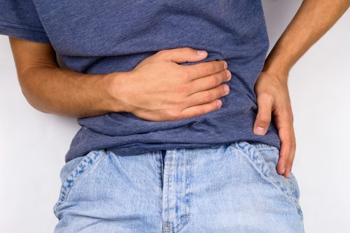 Person in blue shirt and jeans holding their stomach and hip, likely in pain.