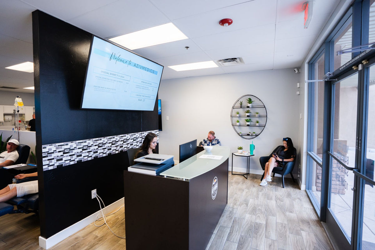 Reception area with patients, a desk, and a television screen. Black and white decor with wood-look flooring.