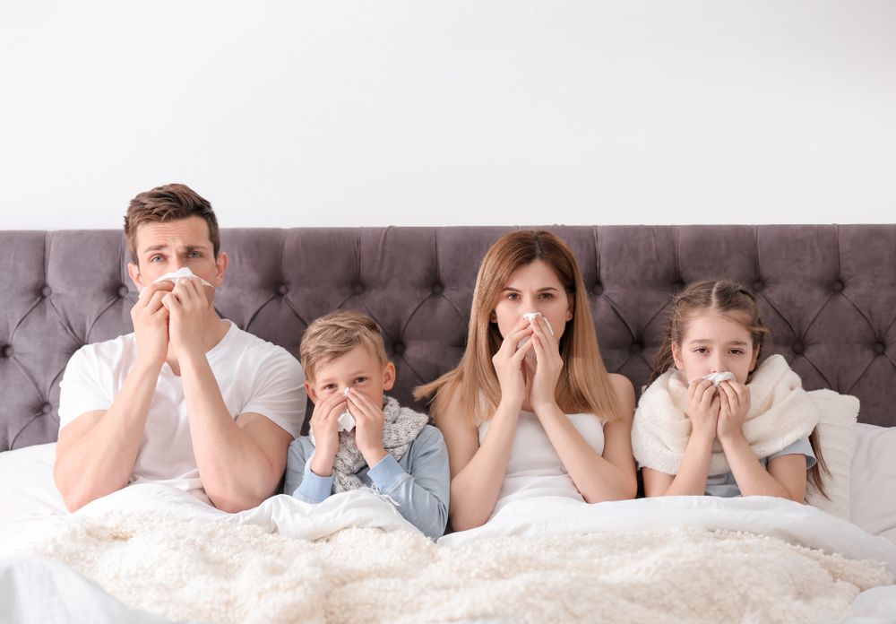 Family in bed, blowing their noses.
