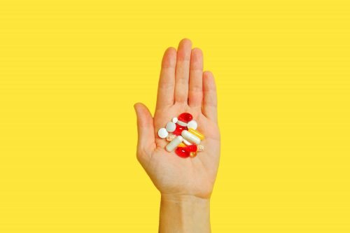 Hand holding a collection of pills and capsules against a yellow background.
