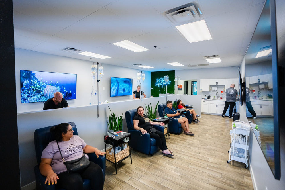 People relax in an IV therapy clinic with recliners and screens showing nature scenes.
