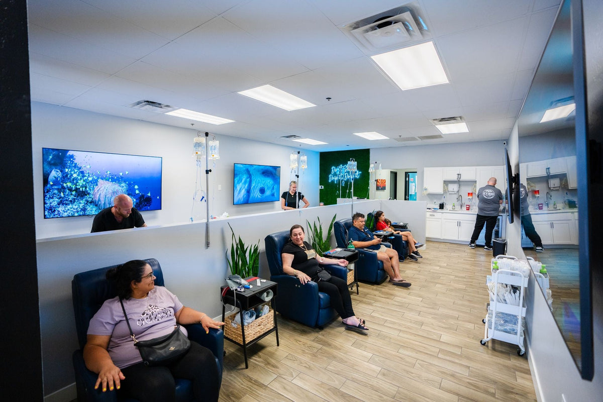 People relax in an IV therapy clinic with recliners and screens showing nature scenes.