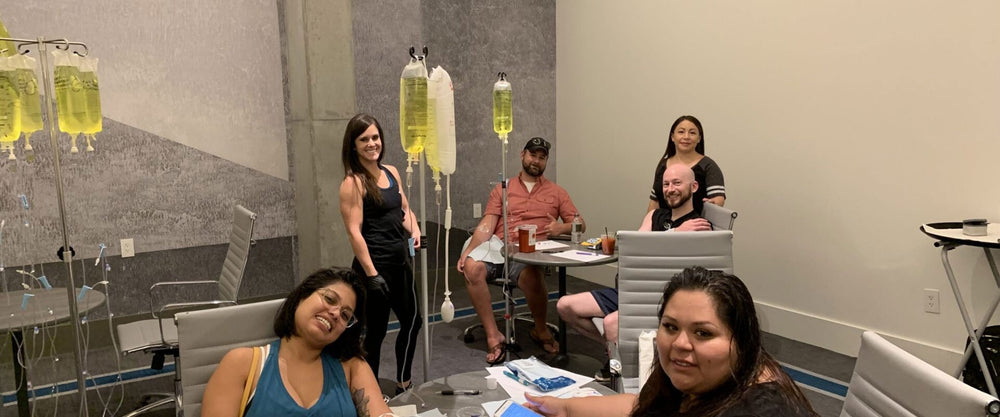 People in a room with IV drips; some are seated at tables smiling.