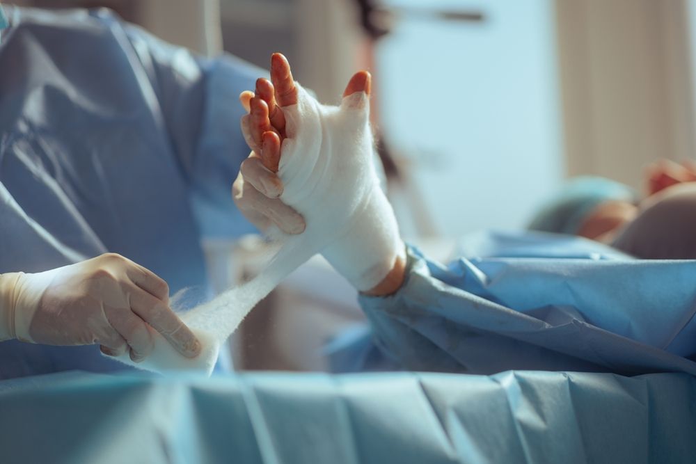 Person in gloves wrapping a hand with white bandage in a sterile, blue-draped setting.