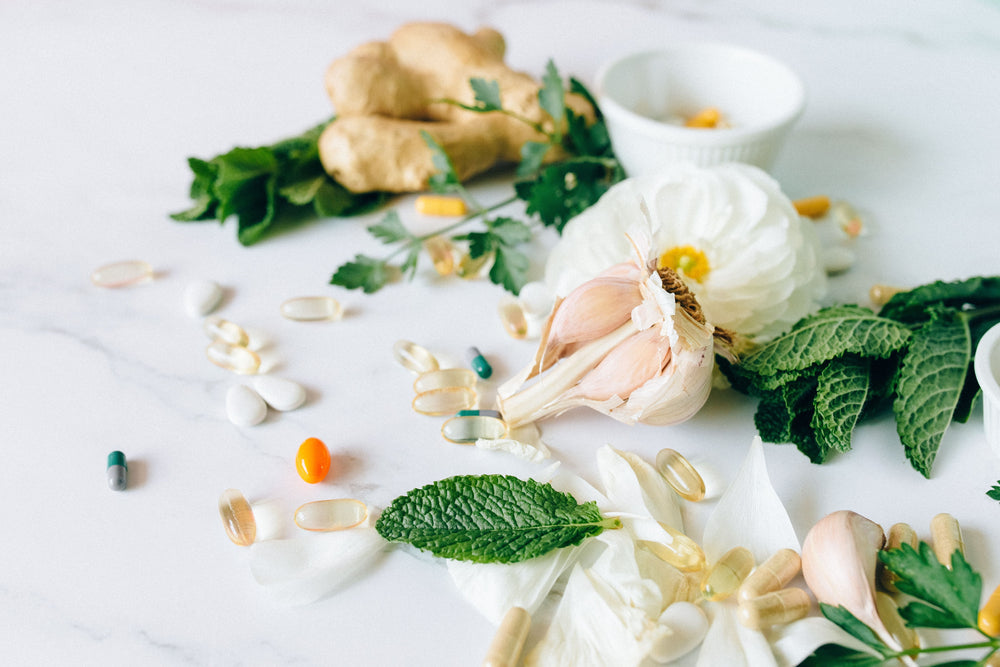Ginger, garlic, mint, and pills on a white surface, representing health and wellness.