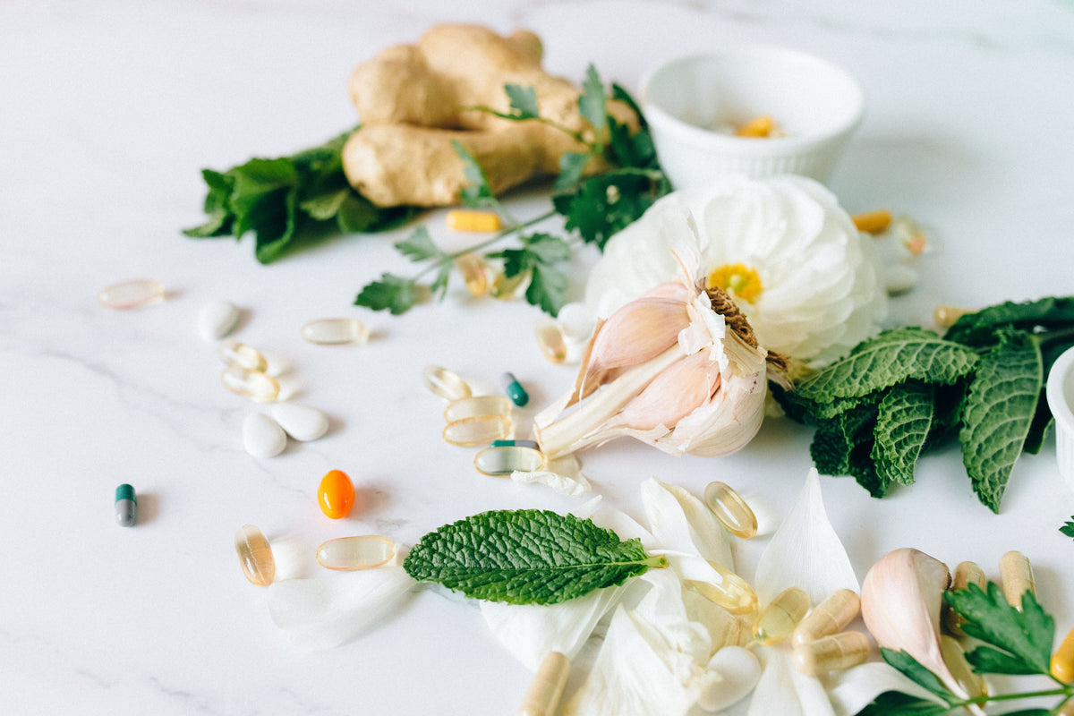 Ginger, garlic, mint, and pills on a white surface, representing health and wellness.