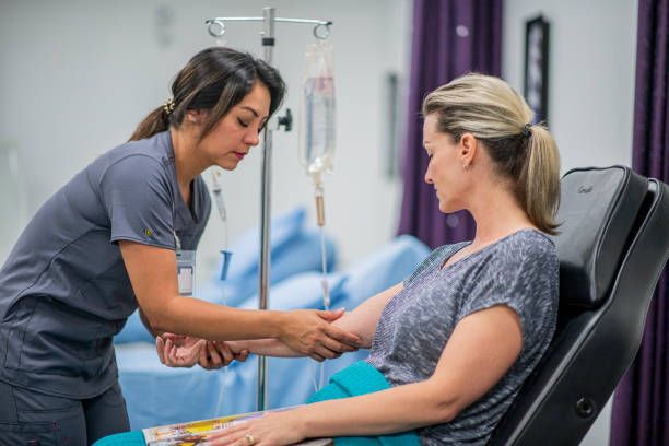 Nurse setting up IV for a patient seated in a medical chair.