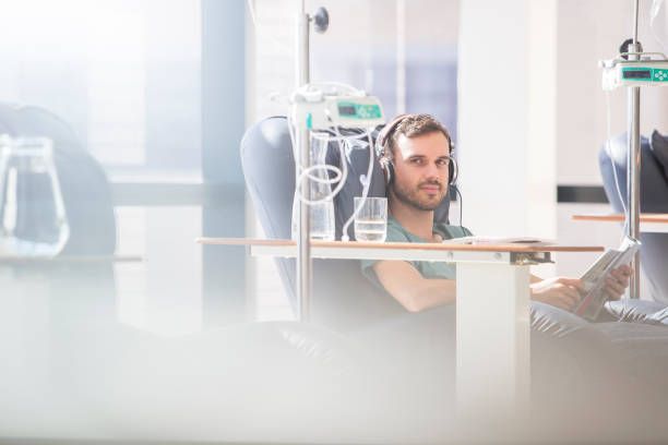 Man in headphones receiving IV treatment, seated, looking towards camera. Medical equipment visible.