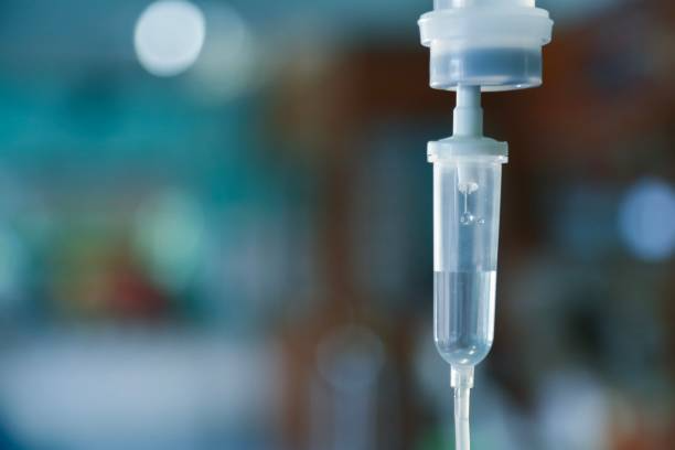IV drip, clear fluid flowing through a plastic tube. Blurred background.