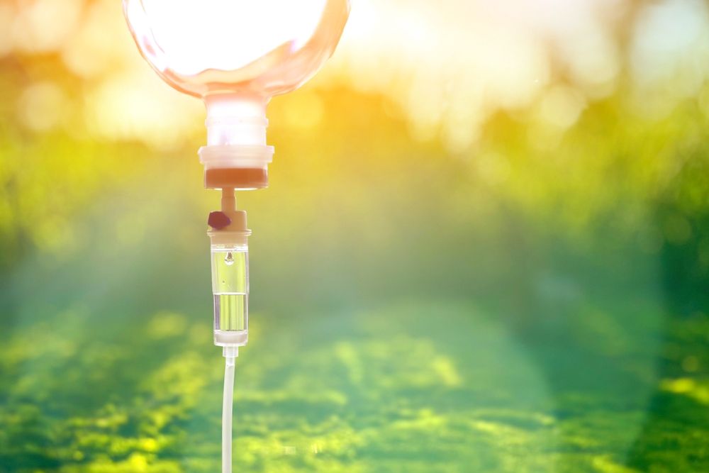 IV drip bag against a blurry green background with bright sunlight.