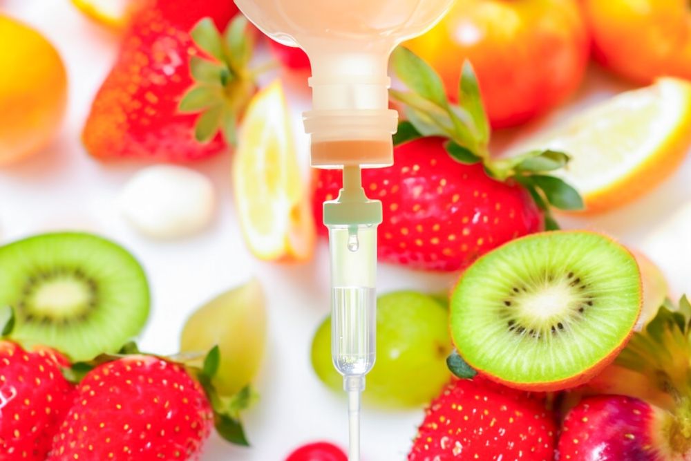 IV drip with fruit: strawberries, kiwi, orange, and grapes, suggesting a vitamin infusion.