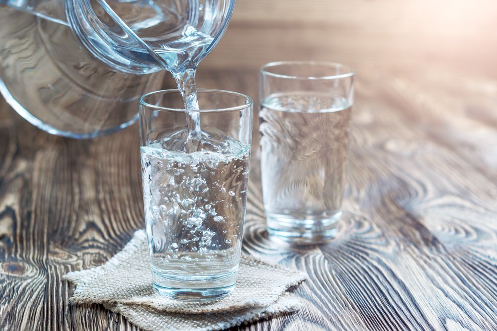 Water being poured from a pitcher into a glass on a wooden surface.