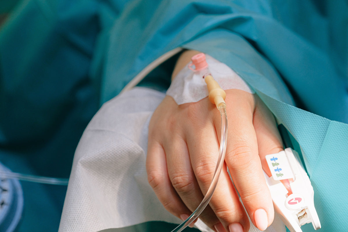Hand with IV line inserted, draped with medical fabric, likely in a hospital setting.