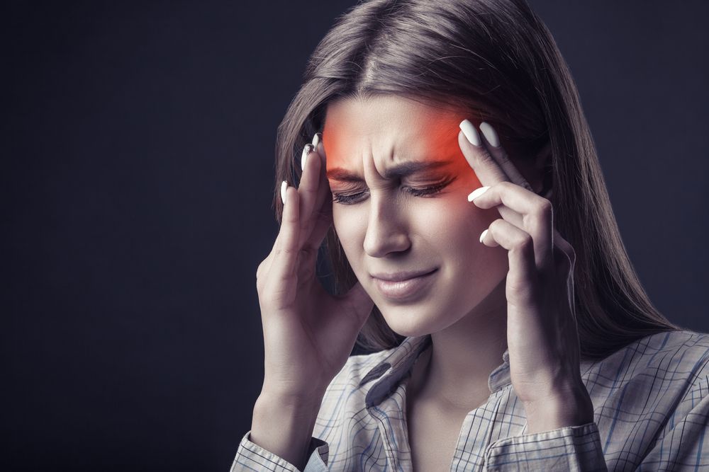 Woman with a headache, red highlight over forehead, eyes closed, hands on temples.