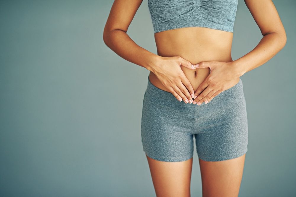 Woman in workout clothes makes heart shape over abdomen.