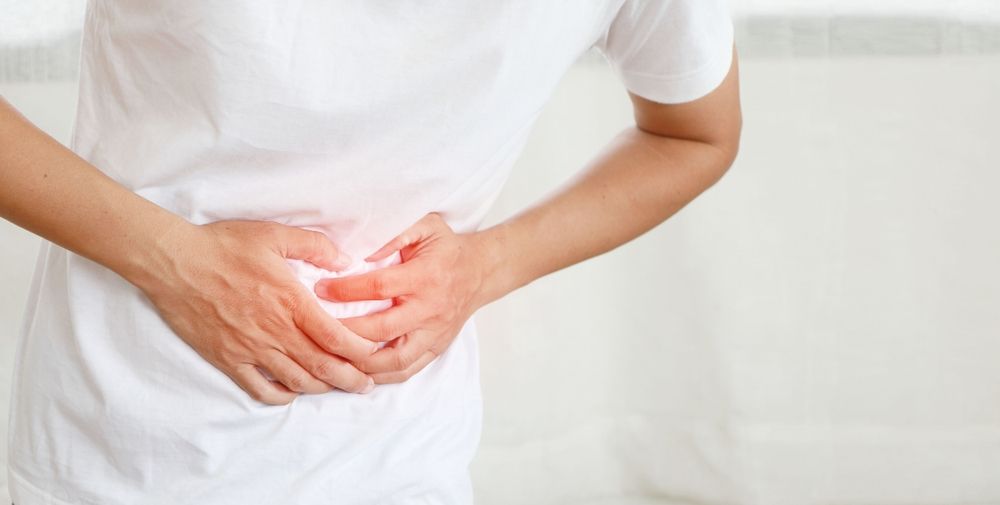 Person in white shirt clutching stomach, indicated pain.