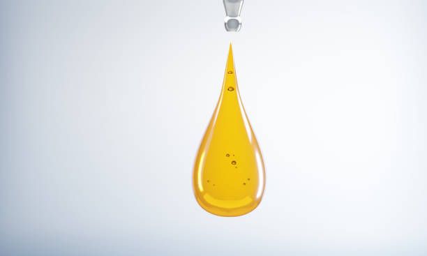 Yellow liquid drop falling from a metal spout.