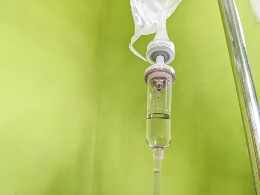 IV drip bag with clear fluid, hanging against a green wall, stainless steel pole.