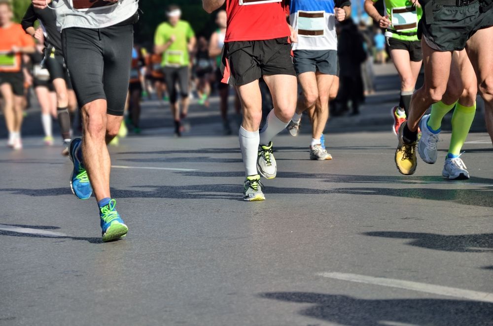 Runners in a marathon, wearing shorts and running gear on a paved road.