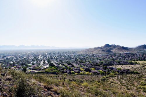 View of a city sprawling between a desert landscape and mountains under a bright sky.