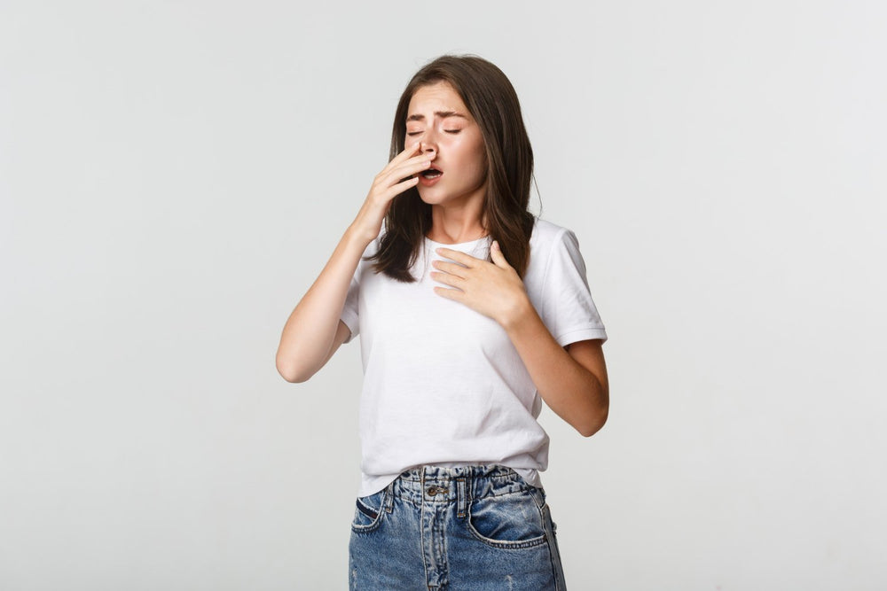 Woman experiencing an allergic reaction, eyes watering, hand on chest, covering nose.