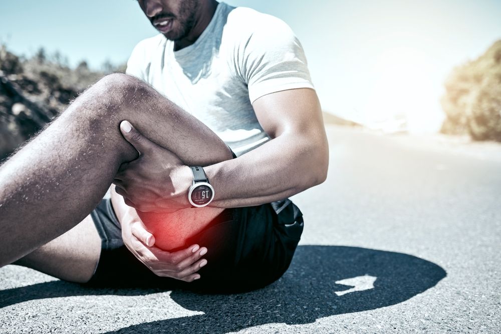 Man sitting on road, holding knee in pain, red highlight.