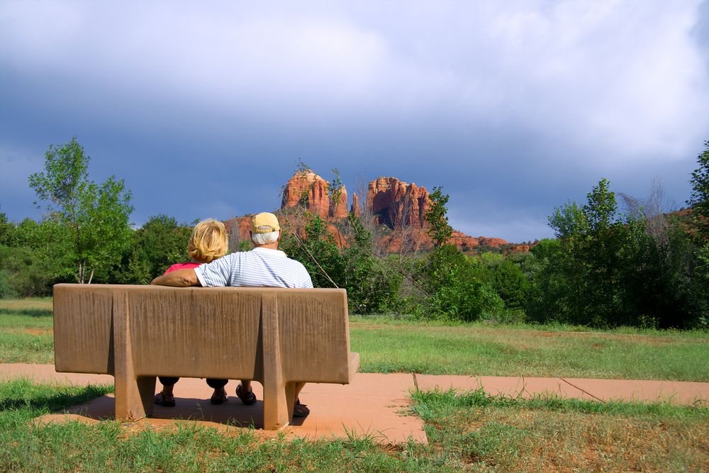 Couple sitting on a park bench, looking at red rock formations under a cloudy sky.