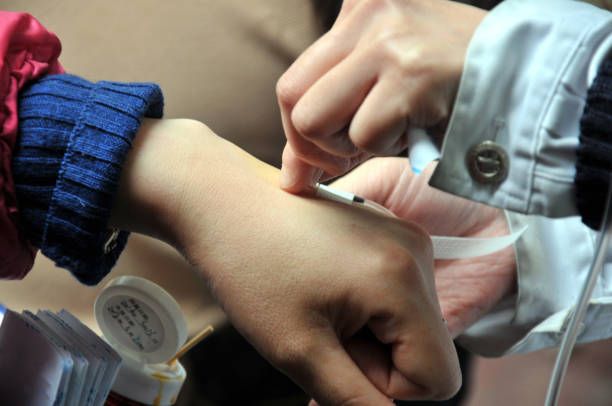 Person's arm receiving an intravenous infusion. Another person's hand inserts the IV.