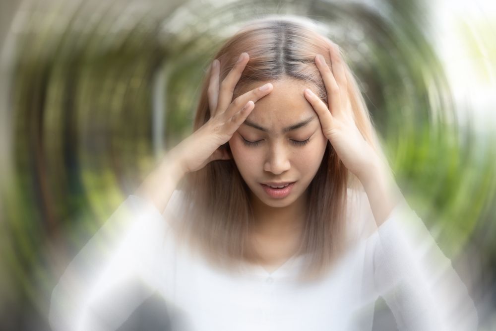 Woman holding head, eyes closed, with blurred vision suggesting dizziness.