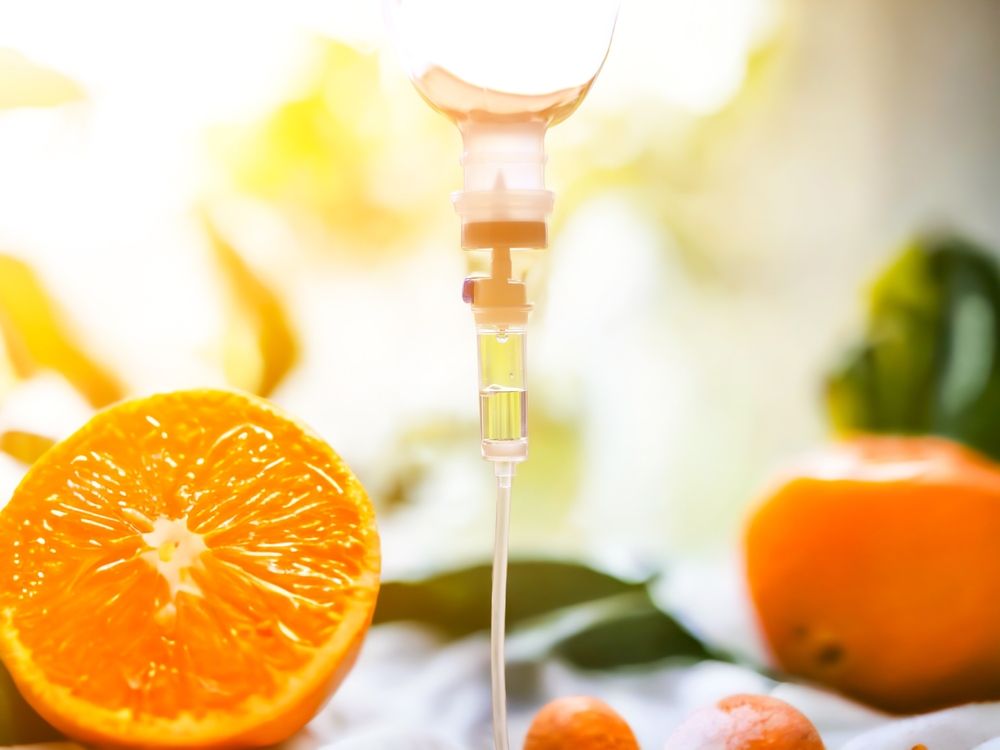 Orange fruit with IV drip, possibly vitamin C infusion, against a bright background.