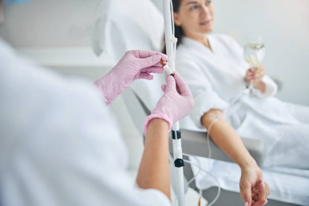 Nurse adjusting IV line for patient in a white robe.