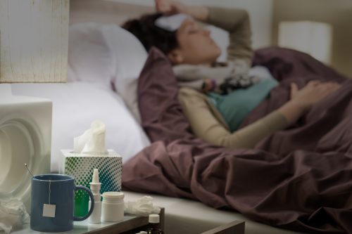 Person in bed, possibly ill, with tissues, medication, and a mug on the nightstand.