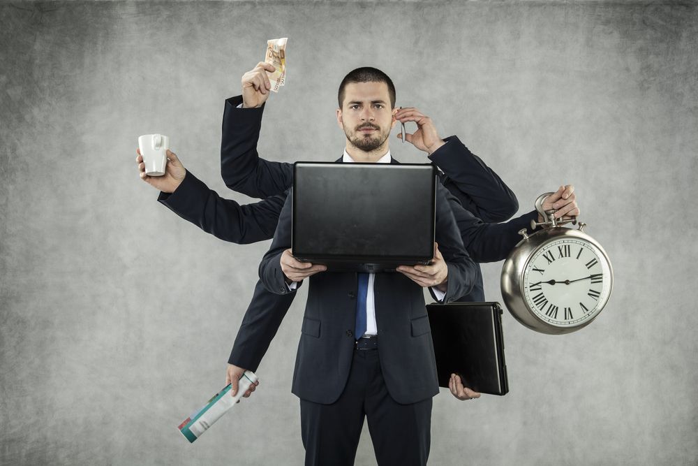 Man in suit with multiple arms, juggling laptop, money, phone, coffee, clock, and briefcase.
