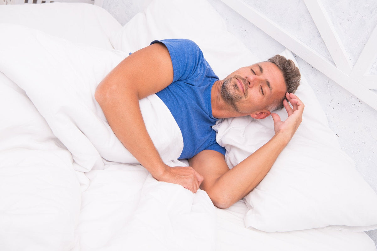 Man sleeping in bed, white bedding, blue shirt.