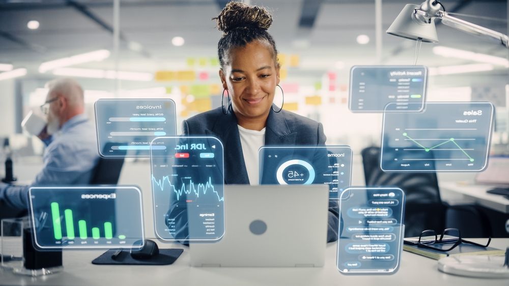 Woman working on laptop, surrounded by floating data screens in a modern office.